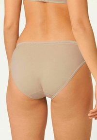 Beige Baumwollmischungslang mit glatter Textur, hoch geschnittenen Beinausschnitten und zarter gestickter Borte entlang des Bundes und der Beinabschlüsse.