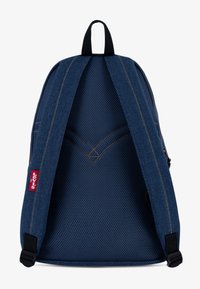 Denimryggsäck med en strukturerad blå tyg, nätpanel på baksidan och tan sömmar. Inkluderar justerbara axelremmar och en röd Levi's logotypetikett.