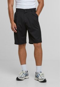 Shorts noirs ajustés en tissu lisse, dotés d'une fermeture à bouton sur le devant, de deux poches latérales et d'une coupe droite.