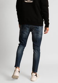 Tummansiniset, kapealahkeiset farkut, joissa viiden taskun muotoilu ja lievää haalistumista. Yhdistetty mustaan huppariin ja valkoisiin lenkkareihin.