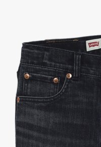 Vaqueros de mezclilla azul oscuro con remaches de cobre, un pequeño bolsillo frontal y una etiqueta roja y blanca de Levi's en la cinturilla.