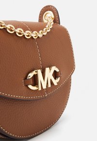 Piccola borsa in pelle marrone con tracolla in catena dorata e prominente chiusura con logo "MK" in oro sulla patta anteriore.