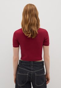 Rotes, geripptes Kurzarmoberteil mit Cropped-Design, kombiniert mit dunklen Jeans, die über helle Nähte und Gesäßtaschen verfügen.