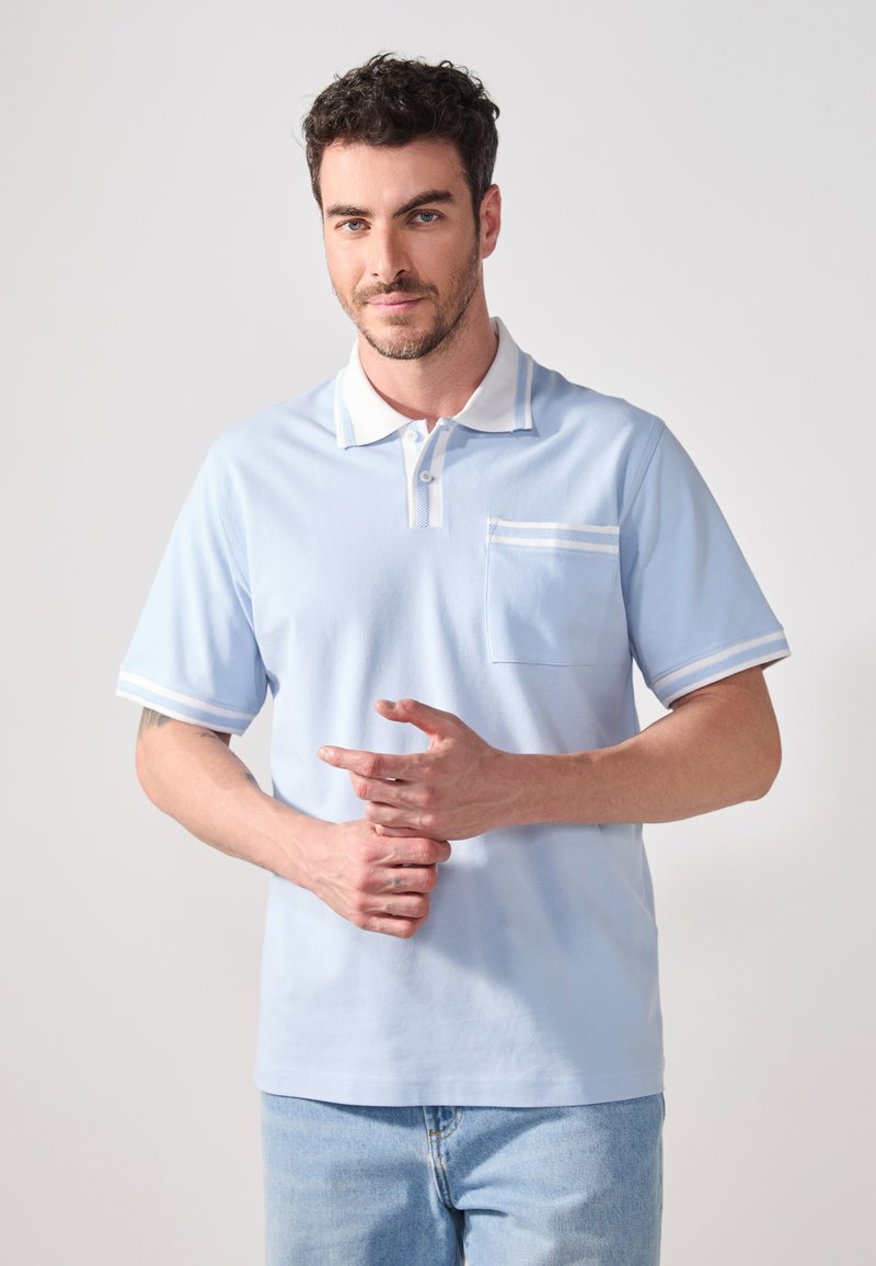 Polo de culoare albastru deschis, fabricat dintr-un material moale, cu un guler alb, accente în dungi pe mâneci și o bijuterie pe piept. Mâneci scurte.