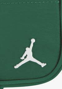 Grønn nylonpouch med en hvit Jumpman-logo. Jevn tekstur med sydd kanter, kompakt rektangulær form, egnet for små gjenstander.