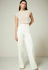 Top beige attillato con maniche corte abbinato a pantaloni bianchi a vita alta e gamba larga. Tessuto morbido; dettagli di cucitura sottili; design minimalista.