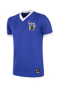 Jersey azul con escote en V, puños y ribete blancos. Presenta una imagen de un futbolista celebrando en el pecho. Incluye un parche de logo en la parte inferior.