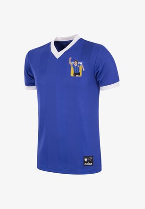 Maillot bleu avec un col en V, des poignets et des bordures blanches. Présente un graphique d'un footballeur célébrant sur la poitrine. Comprend un écusson de logo en bas.