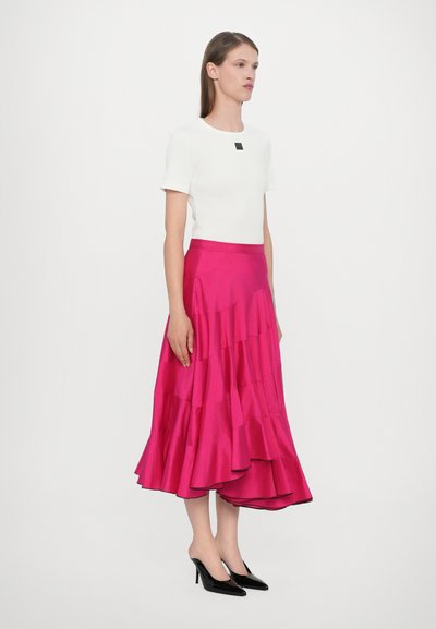 Chemise blanche ajustée avec un accent noir carré et une jupe en satin rose à volants. Des escarpins noirs à bout pointu complètent la tenue.