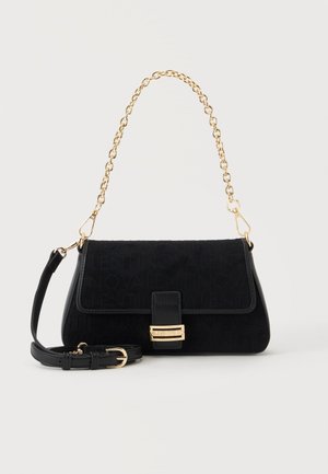 Schwarze Schultertasche mit goldener Kettenhenkel, abnehmbarem schwarzem Riemen und goldenem Verschluss an der Vorderklappe vor hellem, einfarbigem Hintergrund.