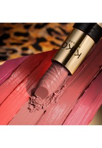 Rouge à lèvres avec étui doré et noir étalé sur plusieurs teintes d'échantillons de rouge à lèvres roses et rouges sur une surface.
