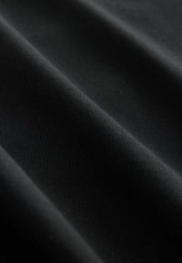 Svart tyg med ribbat mönster, som visar mjuka draperingar och veck, vilket framhäver släthet och djup i färgen.