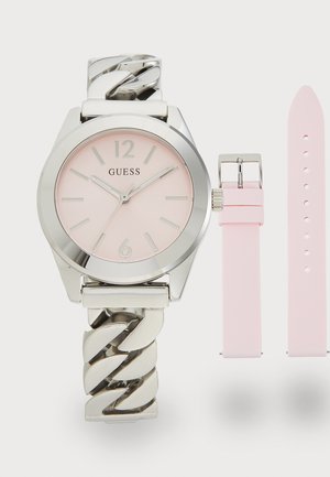 Montre-bracelet argenté avec un cadran rose, dotée d'un bracelet en maillons et d'un bracelet en silicone rose amovible. Chiffres arabes aux positions 12 et 6.