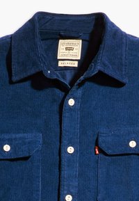 Camisa de pana azul marino con cuello extendido, cierre frontal con botones y dos bolsillos en el pecho; cuenta con una etiqueta que dice "Levi Strauss & Co." y "Relaxed."