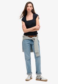 Sort kortærmet top med firkantet halsudskæring, denim jeans, grå sweater knyttet om livet og hvide sneakers med sorte accenter.