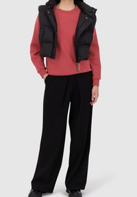 Chaleco negro acolchado sobre sudadera rosa, combinado con pantalones negros holgados. Diseño sencillo, textura suave y colores neutros.