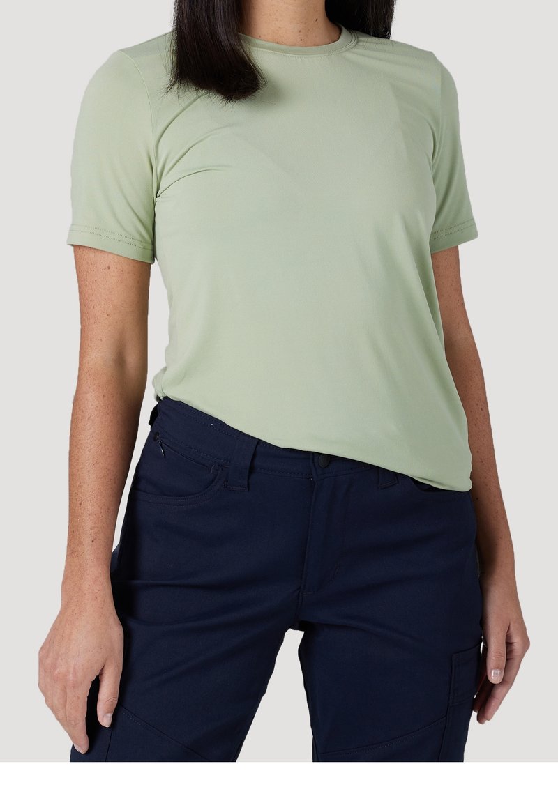 Maglietta fitted verde chiaro con maniche corte, realizzata in materiale morbido, abbinata a pantaloni blu scuro con tasche e un taglio classico.