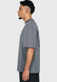 Grå bomulds t-shirt med korte ærmer, afslappet pasform, med en tekstgrafik på højre ærme. Glat tekstur, enkelt design.