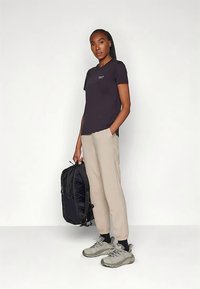 Čierne tričko, béžové nohavice, sivé tenisky. Model drží čierny batoh. Jednoduchý dizajn, hladká textúra, ležérny strih.