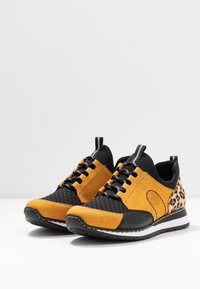 Sneakers med en kombination av gul syntetisk mocka och svart texturerat material, med en leopardmönstrad accent, svarta snören och en vit sula.