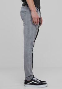 Jeans grises con detalles desgastados y un panel negro contrastante a lo largo del costado, combinados con zapatillas en blanco y negro.