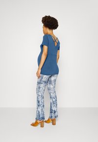 Top azul de manga curta com detalhe nas costas em cruz, combinado com calças flare em tie-dye nas cores azul e branco. Sandálias de salto bloco castanhas.