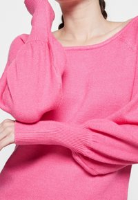 Rosa Strickpullover mit einem lockeren, runden Ausschnitt und puffartigen Ärmeln. Der Stoff wirkt weich mit einer gerippten Textur an den Bündchen.