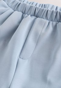 Tissu bleu clair en gros plan montrant une ceinture élastique et un détail de poche avant sur un matériau doux et lisse.