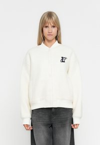 Veste en polaire blanche raccourcie avec fermeture à boutons, poignets côtelés et poches latérales. Présente un logo navy sur la poitrine gauche.