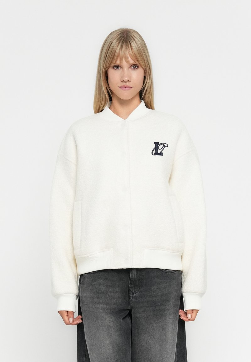 Veste en polaire blanche raccourcie avec fermeture à boutons, poignets côtelés et poches latérales. Présente un logo navy sur la poitrine gauche.