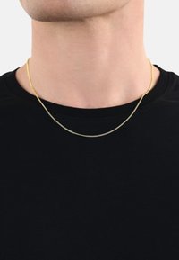Collar de cadena en tono dorado descansando sobre una camiseta negra, con un diseño delicado y delgado, y una textura suave con un brillo sutil.