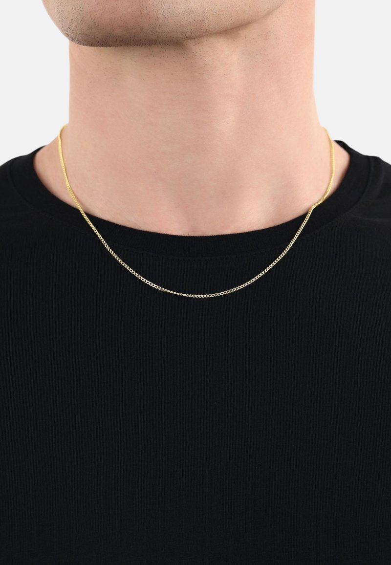 Collar de cadena en tono dorado descansando sobre una camiseta negra, con un diseño delicado y delgado, y una textura suave con un brillo sutil.
