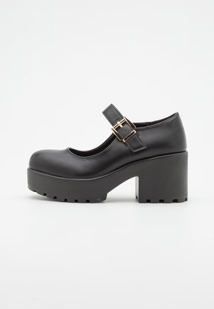 Bottines Mary Jane en cuir noir avec un bout arrondi, une sangle réglable, une boucle dorée et un talon plateforme épais avec une semelle en caoutchouc texturée.