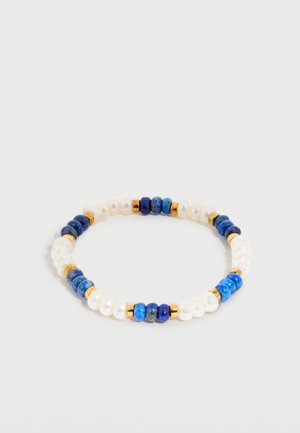 Bracelet élastique avec des perles alternées bleues, blanches et dorées disposées selon un motif répétitif sur un fond clair.