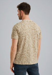 Beige kortærmet t-shirt med et brunt abstrakt mønster. 100% bomuldsstof med en afslappet pasform, rund halsudskæring og glat tekstur.