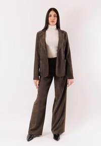 Completo in velluto a coste marrone con tasche grandi, blazer attillato e pantaloni a gamba larga. Abbinato a un dolcevita bianco e scarpe nere con punta.