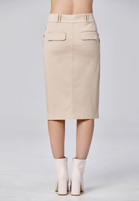 Jupe crayon beige à la silhouette ajustée, avec deux poches arrière et une texture lisse. Assortie à des bottines blanches.