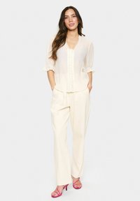 Weiße, strukturierte Bluse mit Rüschensäumen, Knopfleiste, kombiniert mit cremefarbenen Hosen und rosa Riemchenheels. Einfaches, lässiges Design.