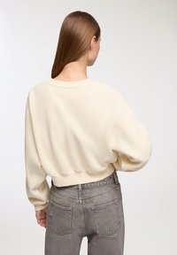 Felpa over-sized color crema con orlo e polsini a costine, abbinata a jeans in denim grigio a vita alta. Texture liscia, vestibilità comoda.