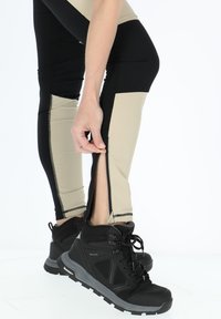 Flerfärgade leggings med svarta och beige paneler och dragkedjor vid anklarna, i kombination med svarta vandringsskor. Slätt och elastiskt material.