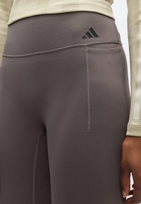 Leggings cinzentas de cintura alta com uma textura suave, apresentando detalhe de logótipo preto, costura subtil e um bolso lateral.