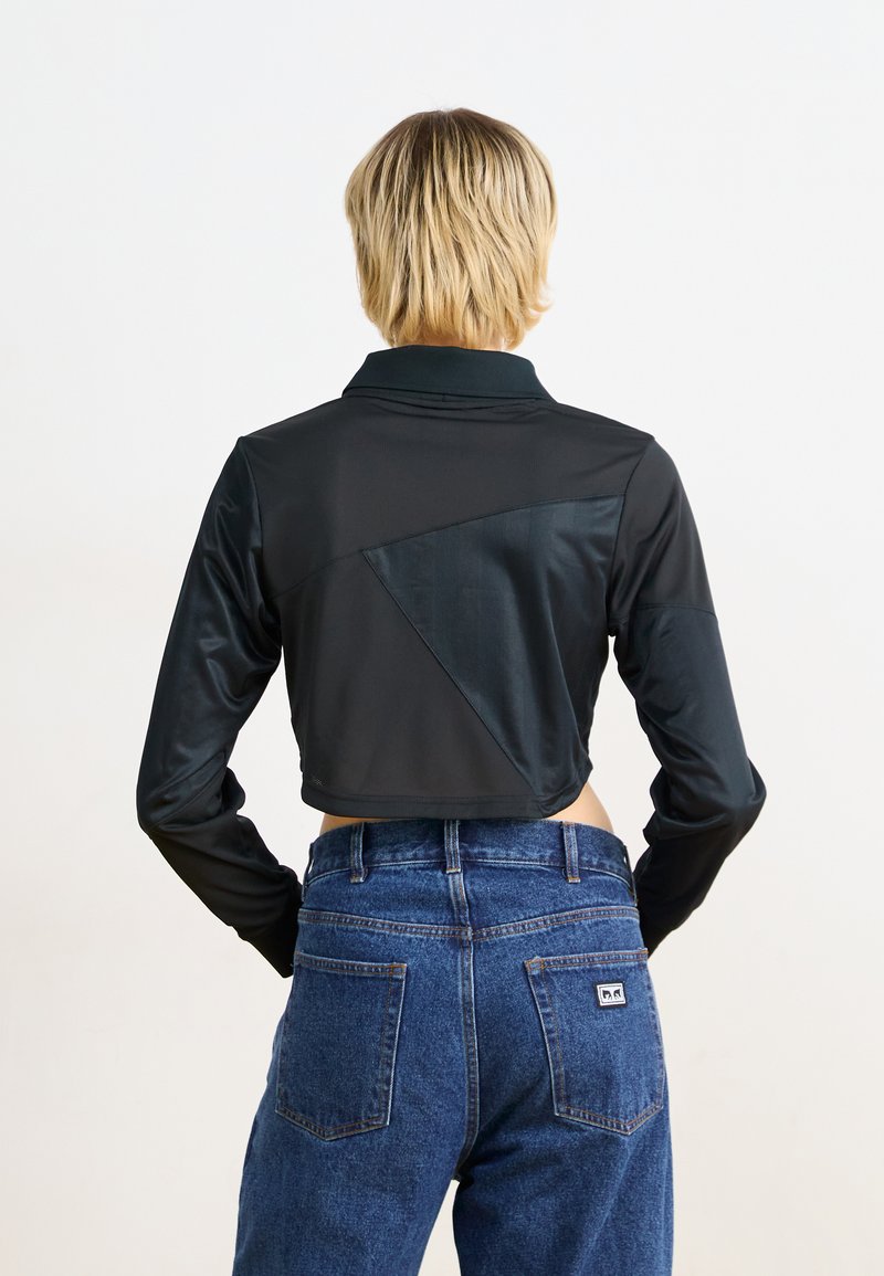 Giubotto nero corto con maniche lunghe, caratterizzato da una texture geometrica e colletto. Abbinato a jeans blu a vita alta, con tasche posteriori.
