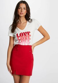 Maglietta bianca a V con stampa "LOVE" in rosa e rosso, abbinata a una mini gonna rossa con due bottoni decorativi e spacchetti laterali.