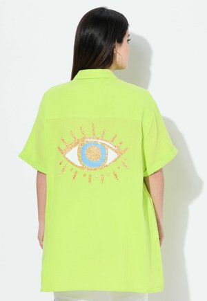 Camisa verde lima de manga corta con un corte oversized, que presenta un gráfico de un ojo brillante en azul y naranja en la parte posterior. Tejido texturizado.