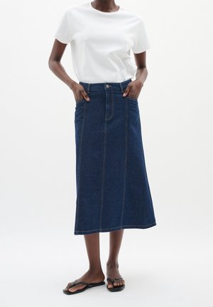 Ciemnoniebieska spódnica dżinsowa o prostym kroju, z przednimi kieszeniami i widocznymi przeszyciami. Połączona z białym T-shirtem z okrągłym dekoltem.