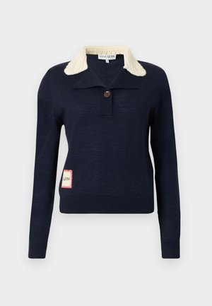 Pull bleu marine à manches longues avec col texturé crème, un bouton simple au niveau du cou, et une petite pièce rectangulaire sur le côté inférieur.