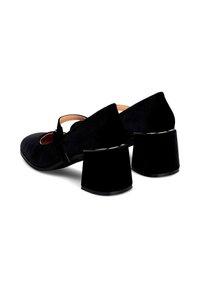 Zapatos Mary Jane de ante negro con punta redonda, una correa con hebilla y un tacón ancho negro. Textura suave con acentos brillantes.
