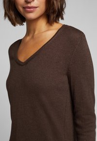 Brązowy sweter w serek wykonany z miękkiego materiału, o dopasowanym kroju i prążkowanych wykończeniach przy dekolcie i mankietach.
