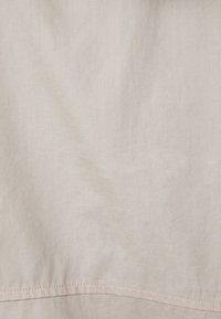 Ljusbeige linne med en mjuk textur, som har en subtil glans och en sydd fåll nederst.