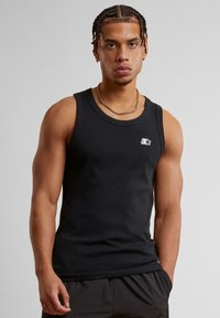 Svart ermeles tanktop laget av bomull, med rund hals og en liten hvit logo på brystet. Jevn tekstur og figursydd design.